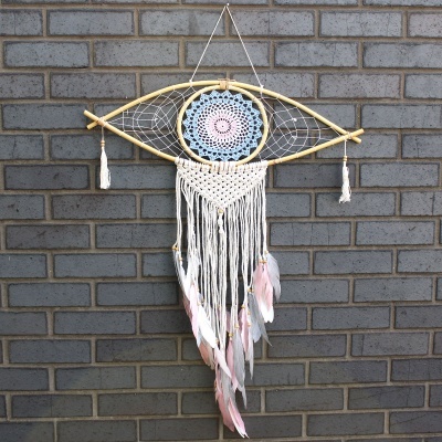Apanhador de sonhos olho com cordas e penas pendurado numa parede de tijolos cinzentos