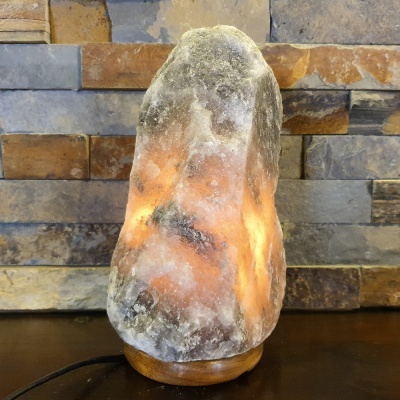 Lâmpada de sal natural iluminada com base de madeira em ambiente com parede de pedra.