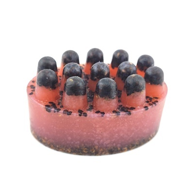 Sabonete artesanal redondo cor-de-rosa com textura bolhosa e pequenos grãos pretos