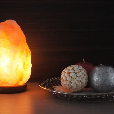 Lâmpada de sal iluminada e velas decorativas num prato prateado sobre superfície de madeira