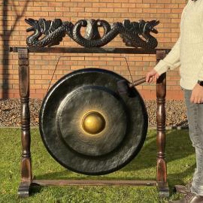 Gongo preto com suporte de madeira esculpido e baqueta na mão de uma pessoa