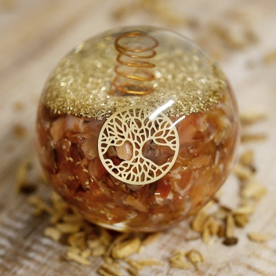 Esfera decorativa transparente com pedras castanhas, mola cobre, textura dourada e emblema de árvore sobre tecido bege com sementes