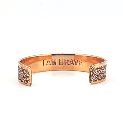 Pulseira cobreada aberta com padrão ornamental nas extremidades e texto interno I AM BRAVE.