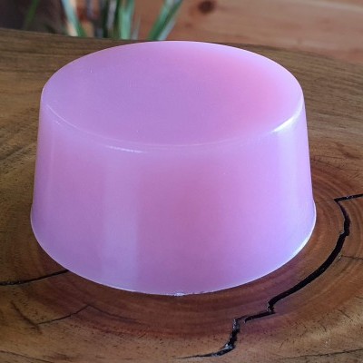 Sabonete sólido cor-de-rosa translúcido sobre superfície de madeira clara