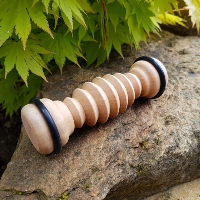 Massajador de madeira claro com aneis pretos sobre pedra