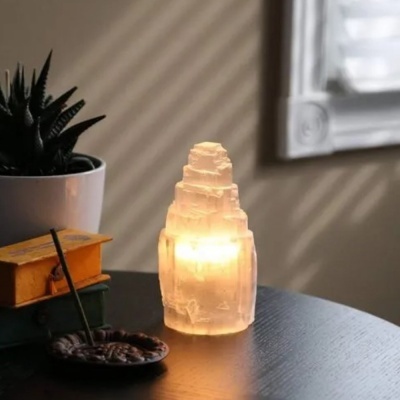 Vela decorativa translúcida em forma de torre com luz quente numa mesa preta com planta suculenta, livros e incenso