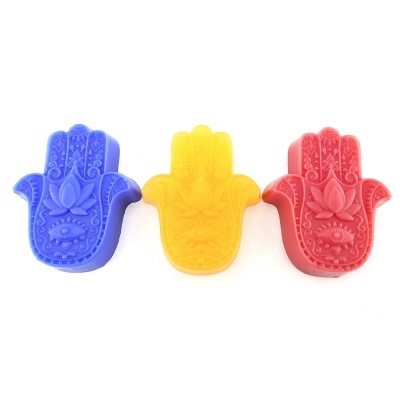 Três sabonetes coloridos em forma de mão de fatima com desenhos gravados