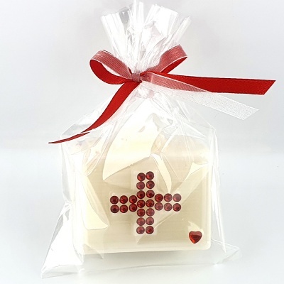 Objeto de cerâmica branca com cruz vermelha embrulhado em saco plástico com fita vermelha.