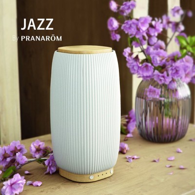 Difusor de aroma branco com base e tampa em madeira numa superfície de madeira com flores lilases