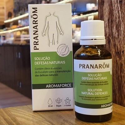 Frasco e caixa do produto Pranarôm Solução Defesas Naturais sobre mesa de madeira