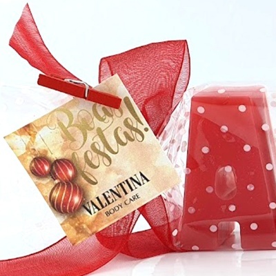 Vela vermelha com pontos brancos embrulhada em celofane com etiqueta 'Boas Festas! VALENTINA BODY CARE'.