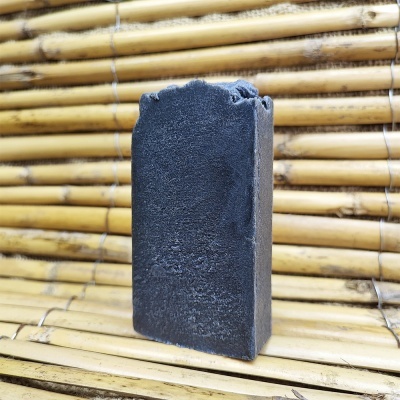 Sabonete preto artesanal com textura rugosa sobre superfície de bambu