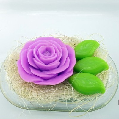 Sabonete decorativo com flor roxa e folhas verdes num prato de vidro