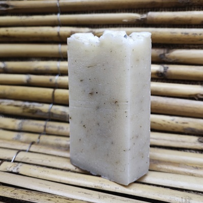 Barra de sabão artesanal branca com partículas escuras, sobre superfície de bambu