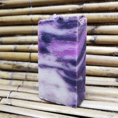 Sabonete artesanal em tons roxo, lilás, branco e preto sobre fundo de bambu