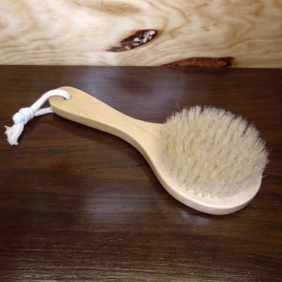 Escova corporal de madeira com cerdas brancas e cordão branco numa superfície de madeira