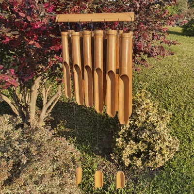 Cata-vento de bambu pendurado num jardim com plantas e relva