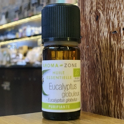 Frasco de óleo essencial de eucalipto numa superfície de madeira com fundo de loja desfocado.