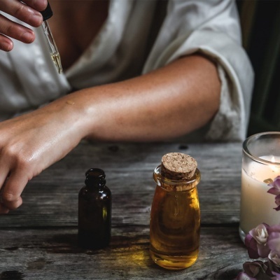 Frascos de vidro com líquidos e mão a aplicar óleo sobre a pele numa mesa de madeira