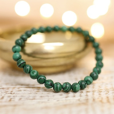 Pulseira de contas verdes com padrão numa superfície de madeira clara com prato dourado ao fundo