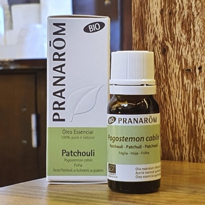 Frasco de óleo essencial Pranarôm Patchouli com embalagem ao lado, sobre mesa de madeira.