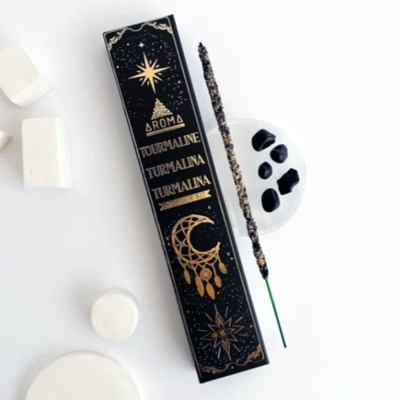 Caixa de incenso preta com texto dourado, palito de incenso e pedras pretas em prato