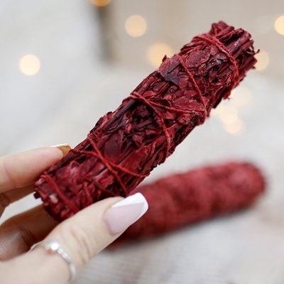 Feixe vermelho de folhas secas amarradas segurado por mãos femininas com unhas pintadas