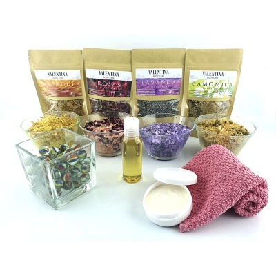 Conjunto de chá de plantas secas, óleo, creme, toalha rosa e bolinhas coloridas em recipiente de vidro