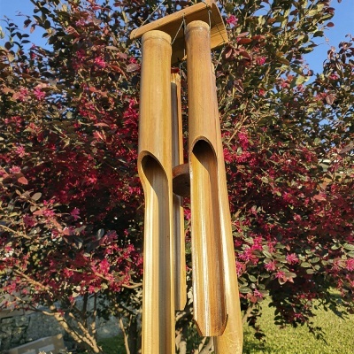 Sino de vento de bambu pendurado junto a uma árvore com folhas e flores vermelhas