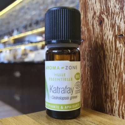 Frasco pequeno de óleo essencial Katrafay com rótulo branco e tampa preta sobre madeira