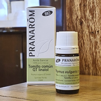 Frasco e embalagem de óleo essencial Pranarôm Tomillo común QT linalol sobre mesa de madeira