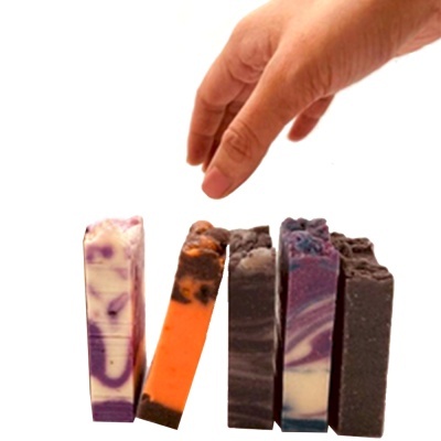 Cinco fatias de sabonete artesanal coloridas e mão a pegar uma delas