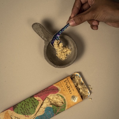 colher com pó amarelo sobre tigela de cerâmica cinzenta ao lado de embalagem colorida aberta