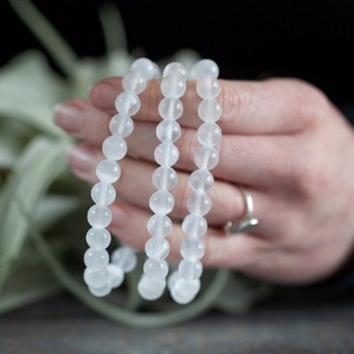 Pulseira de contas brancas translúcidas segurada por mão com anel