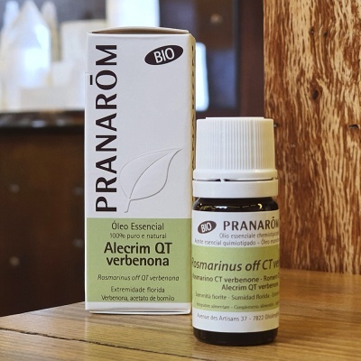 Frasco de óleo essencial Pranarôm Alecrim QT verbenona com caixa ao lado, sobre superfície de madeira