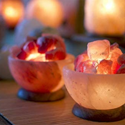 duas taças de sal rosa iluminadas com blocos de sal rosa e bases de madeira sobre mesa de madeira