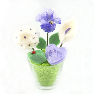 Arranjo decorativo com flores artificiais brancas e lilás, folhas verdes, coração lilás com letras EVA, joaninhas e abelhas, em vaso transparente.