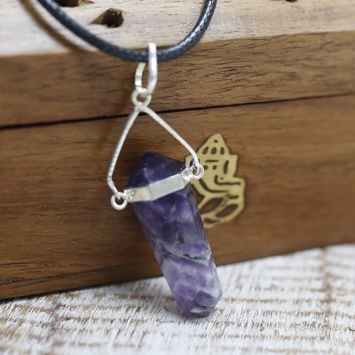 Colar com pendente em pedra ametista roxa e estrutura metálica prateada em fundo de madeira