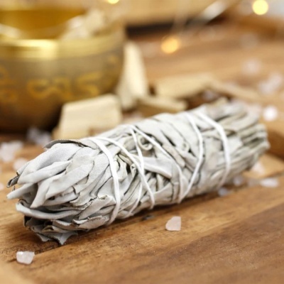 Vara de sálvia branca amarrada sobre madeira com cristais e recipiente dourado ao fundo