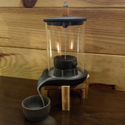 Lâmpada de óleo de vidro com base cinzenta e estrutura de madeira em fundo de madeira.