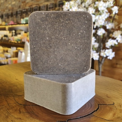 Dois blocos quadrados cinzentos com texturas diferentes sobre mesa de madeira com estante e planta ao fundo