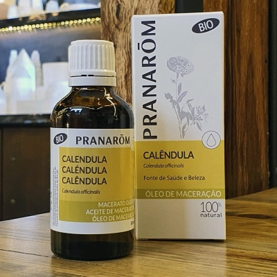 Frasco de óleo de calêndula Pranarôm com embalagem ao lado sobre mesa de madeira