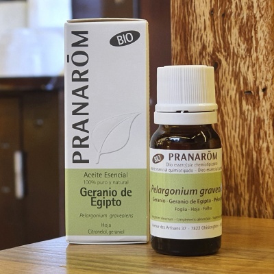 Óleo essencial Pranarôm Gerânio do Egito em frasco de vidro âmbar com embalagem branca e verde sobre mesa de madeira