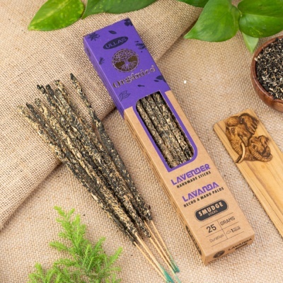 Caixa de incensos de lavanda em papel castanho e roxo, paus de incenso, tecido de juta, folhas verdes e tábua de madeira com gravura de elefantes.