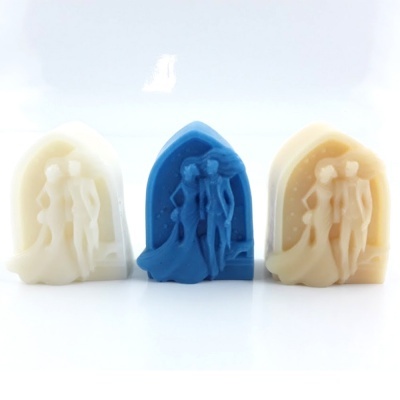 Três esculturas em relevo de um casal, em branco, azul e bege, sobre fundo branco.