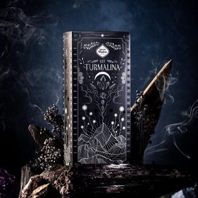 Caixa preta decorada com desenhos brancos de cristais e montanhas, sobre troncos de madeira com ramos secos e fumaça.