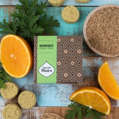 Caixa de produto antimosquito Sagrada Madre com fatias de laranja e folhas verdes sobre mesa de madeira