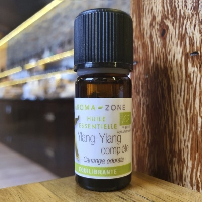 Frasco de óleo essencial Ylang-Ylang com rótulo verde e preto numa mesa de madeira