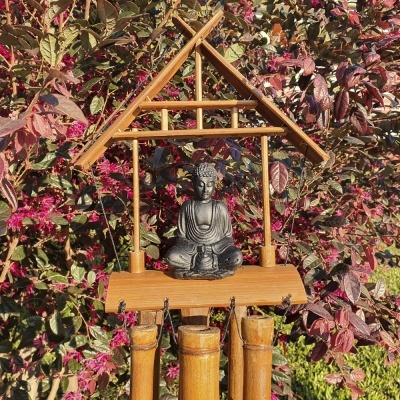 Sino dos ventos com estátua de Buda e tubos em madeira pendurados de fundo folhagem roxa