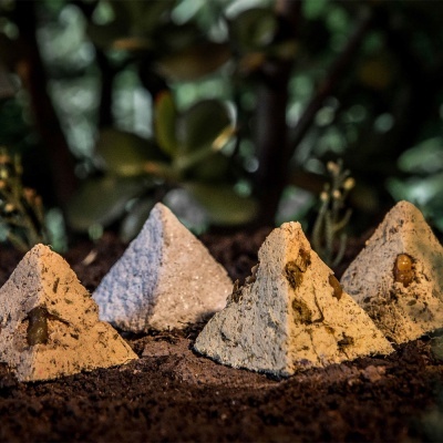 Quatro pequenas pirâmides decorativas em terra com plantas ao fundo